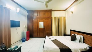 Habitació d'hotel amb llit, armari, escriptori, cadira, televisió i ventilador de sostre.