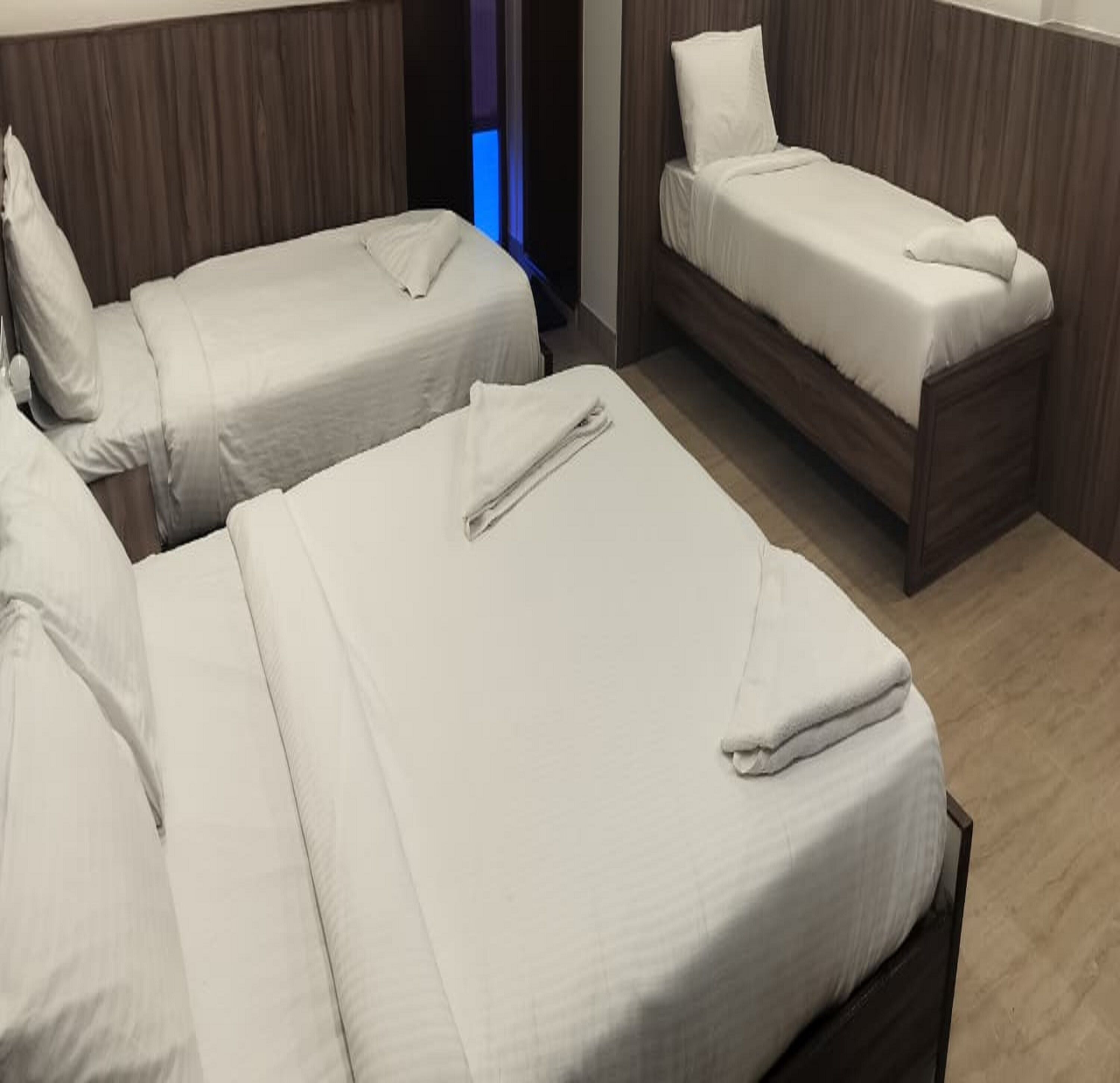 Ett hotellrum med tre sängar placerade i en rad, alla med vita lakan och kuddar.