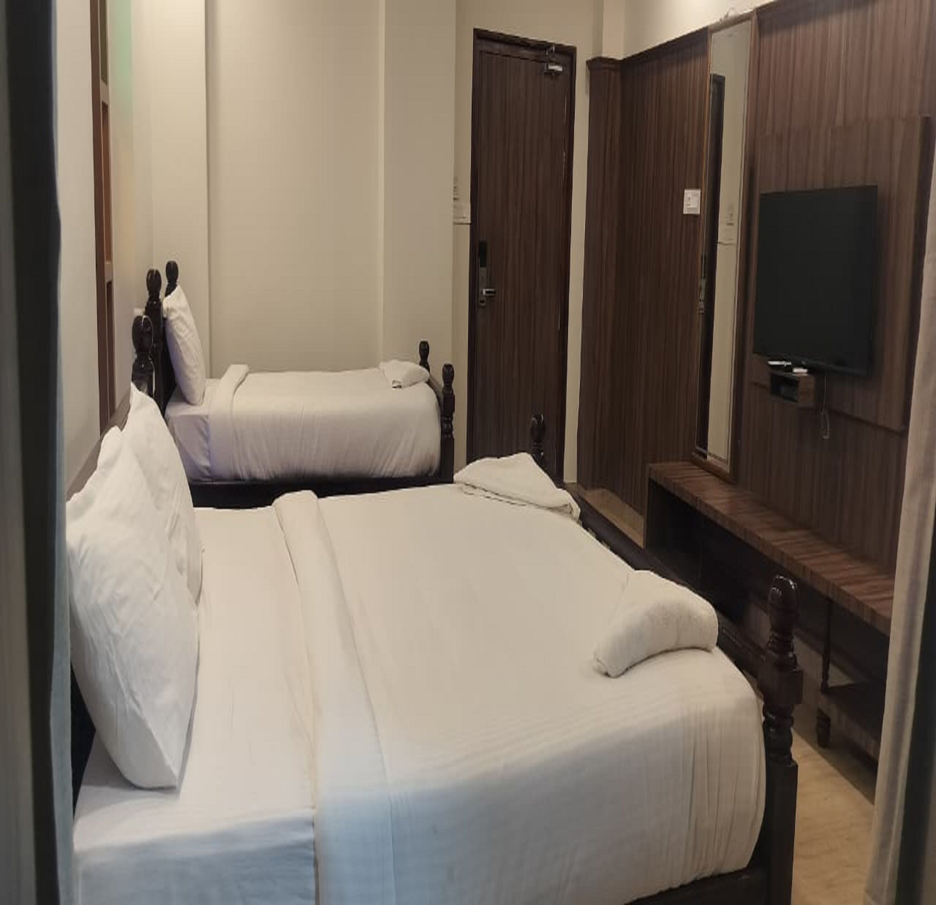 A hotel room with two single beds, a wooden wardrobe, and a television mounted on the wall.
