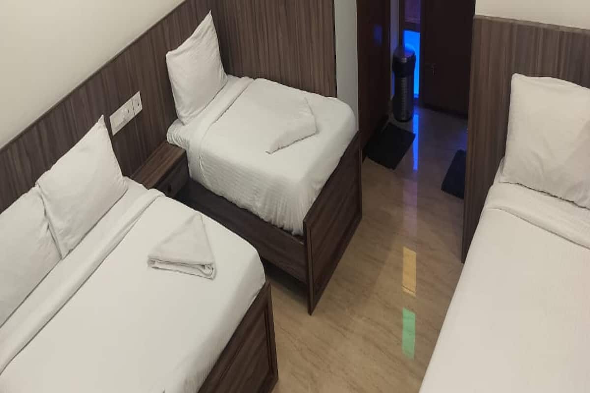 A hotel room with three single beds, wooden headboards, and a tiled floor.