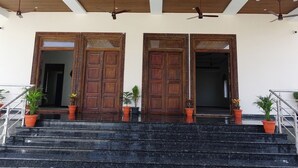 Entrada de um edifício com duas grandes portas de madeira, uma escadaria e vasos de plantas nos degraus.