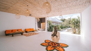 Un interior moderno con techo de madera, cojines anaranjados, una estatua y un estampado floral decorativo en el suelo.