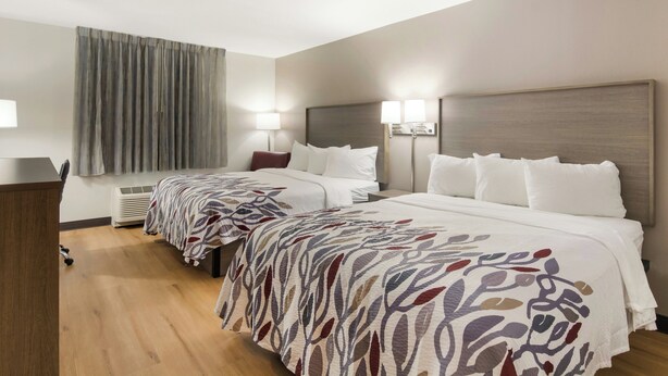A hotel room with two beds, a desk, a lamp, and a window with curtains. - Red Roof Inn Williamsburg North (Williamsburg)