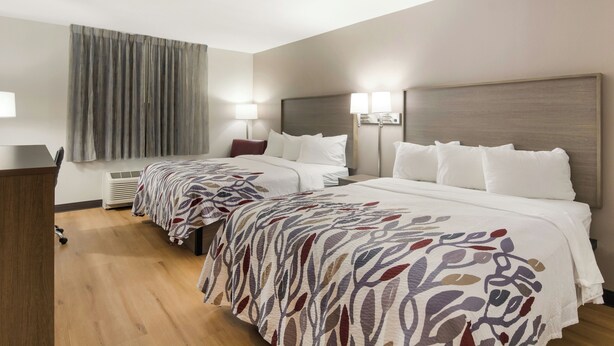 Habitación de hotel con dos camas, un escritorio, una lámpara y una ventana con cortinas.