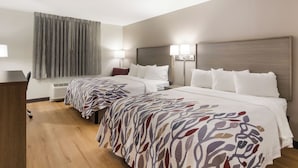 A hotel room with two beds, a desk, a chair, a window with curtains, and a wall-mounted heater. - Red Roof Inn Williamsburg North (Williamsburg)