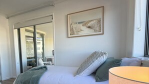 Ein Schlafzimmer mit Bett, Fenster, Gemälde und Lampe.