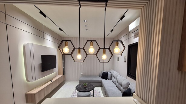 Een moderne woonkamer met een bank, een aan de muur bevestigde televisie en een eettafel met stoelen.