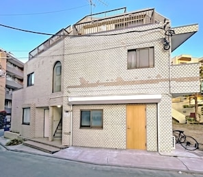 A two-story building with a brick facade, a wooden door, and a small balcony. - Ikebukuro 5 Min by Train | 16㎡ for 1 | Kitchen, Free Laundry | Fast Wi-Fi (板橋区)