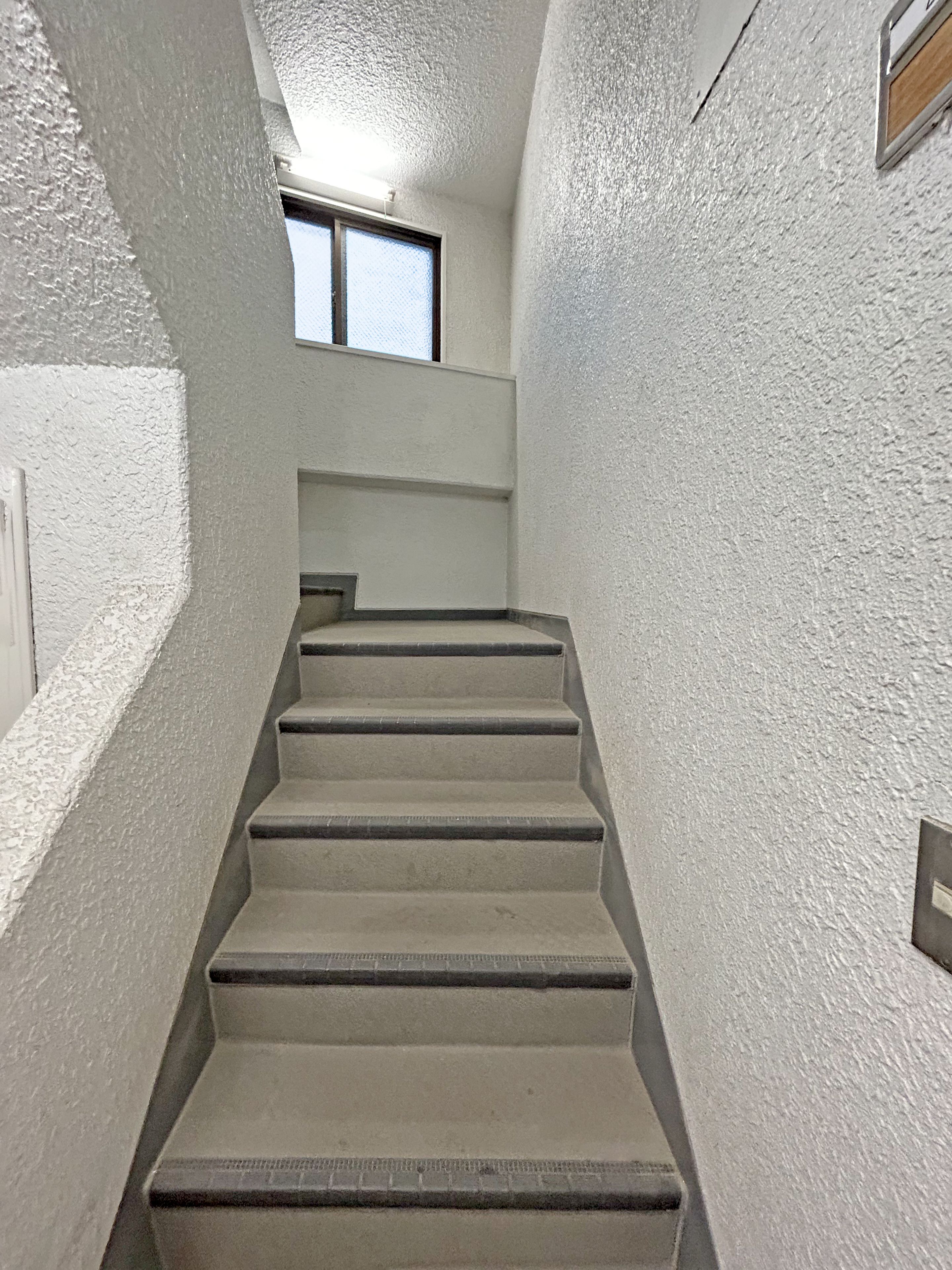 A concrete staircase with a textured wall, a window at the top, and a door on the left.