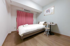 A single bed with a white mattress and pink curtains, a small table with a chair, and a wall-mounted air conditioner. - Ikebukuro 5 Min by Train | 16㎡ for 1 | Kitchen, Free Laundry | Fast Wi-Fi (板橋区)