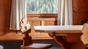 A wooden table with a bench in front of a window with curtains, overlooking a forested area. - Farmhouse apartment with mountain view (Alpbach)