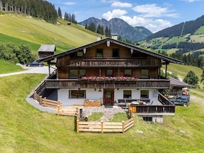 Eine zweistöckige Holzhütte mit Steinunterbau, einem Balkon voller Blumen und Blick auf die umliegenden Berge.