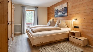 A wooden-paneled bedroom with a bed, bedside tables, and a window with curtains. - Farmhouse apartment with mountain view (Alpbach)