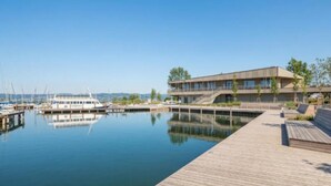 Een pand aan het water met een steiger, een modern gebouw met meerdere verdiepingen, en een boot aan de pier.