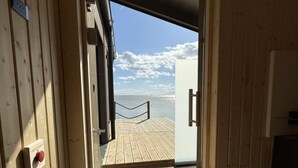 Een geopende deur die uitkomt op een houten terras met uitzicht op de zee.