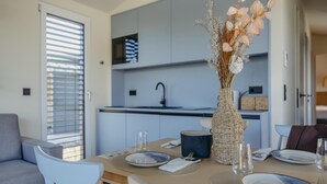 Een moderne keuken met grijze kastjes, een eettafel gedekt met borden en glazen, en een rieten vaas met gedroogde bloemen.