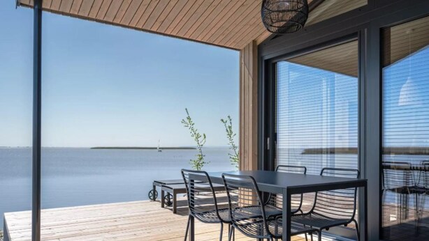 Une terrasse extérieure moderne, dotée d’une table et de chaises, qui offre une vue sur une étendue d’eau paisible.