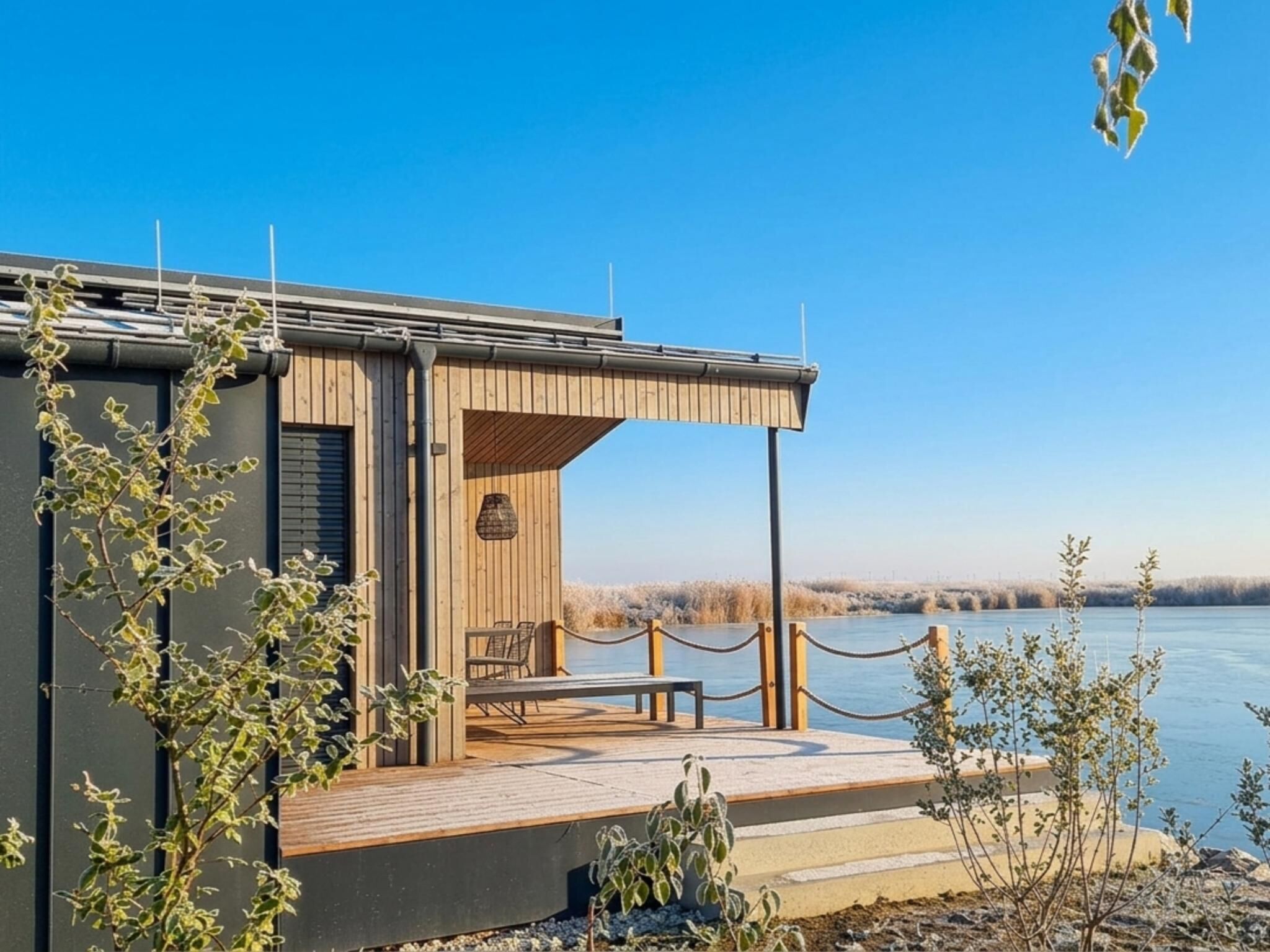 Een modern gebouw met een houten terras en uitzicht op een waterpartij.