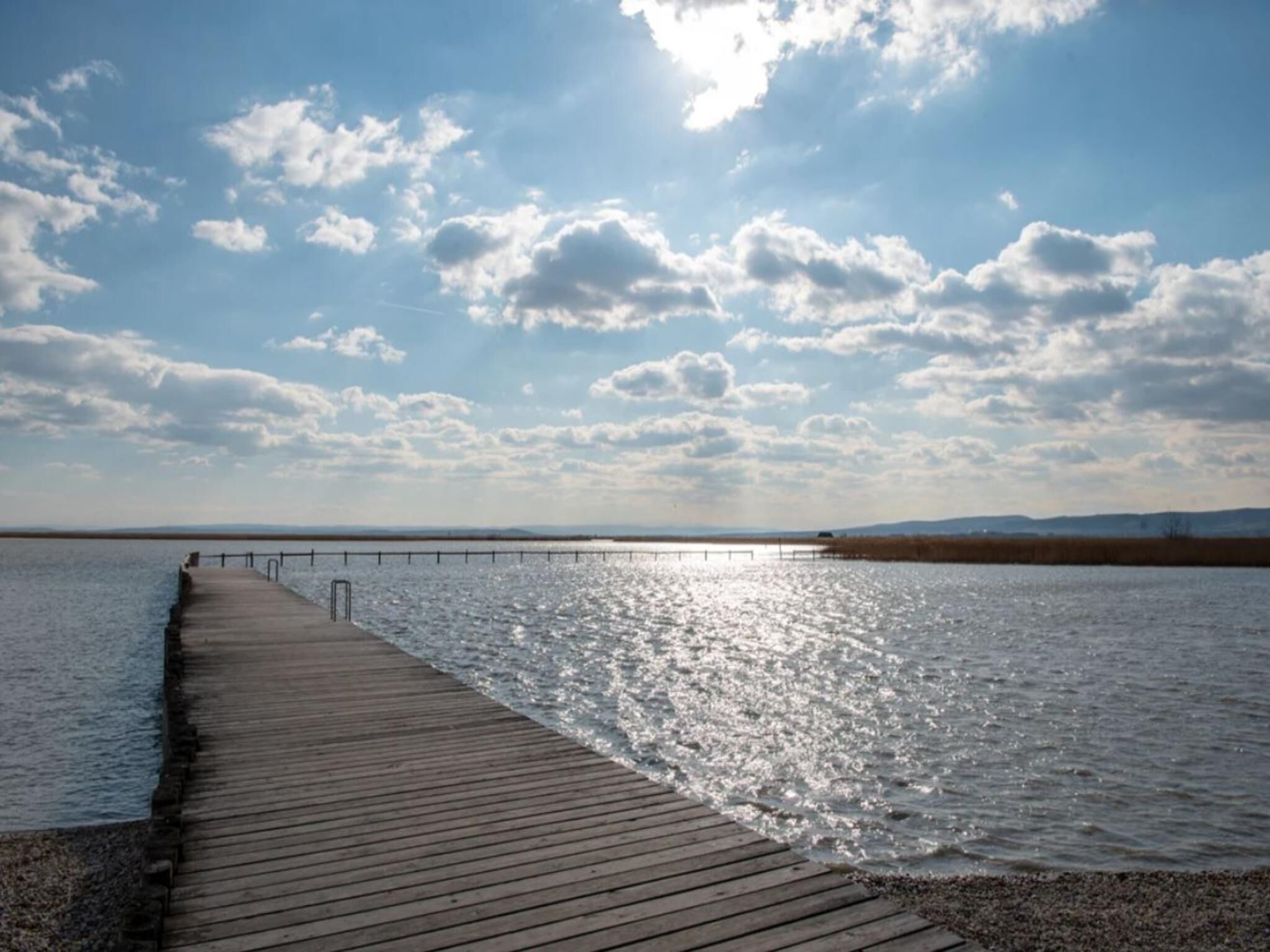 Eine hölzerne Pier, die sich in ruhiges Wasser erstreckt, mit blauem Himmel darüber.