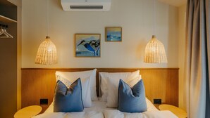 Une chambre d’hôtel avec un grand lit, deux tables de chevet, un luminaire suspendu, un appareil de climatisation et un tableau au mur.