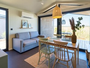 A modern living room with a sofa, dining table, chairs, and a hanging light fixture.