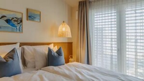 Quarto de hotel com uma cama grande, uma mesinha de cabeceira e uma janela com persianas.