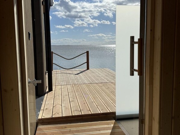 A wooden deck leading to a white door, with a view of the sea and sky.