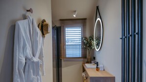 A bathroom with a white robe hanging on the wall, a wooden vanity with a mirror, and a window with blinds. - Wellness guesthouse by a lake with sauna (Breitenbrunn)