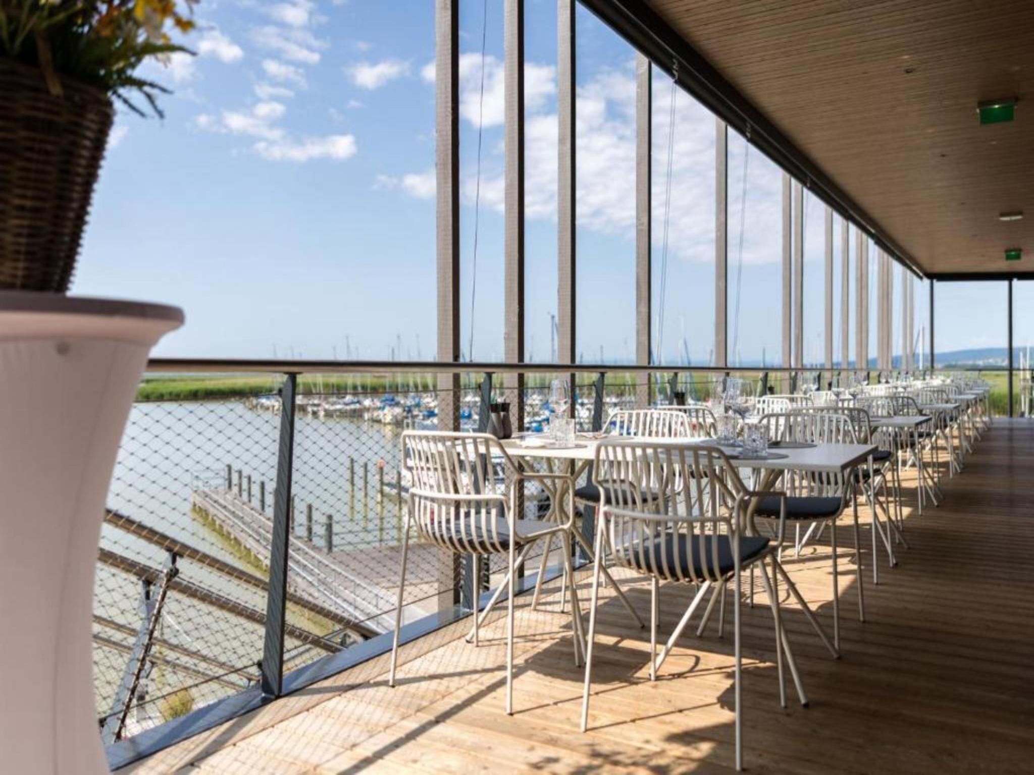 An outdoor terrace with tables and chairs, overlooking a marina with boats.