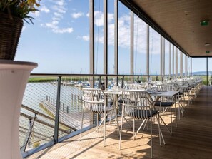 Una terraza al aire libre con mesas y sillas, con vistas a un puerto deportivo con barcos.