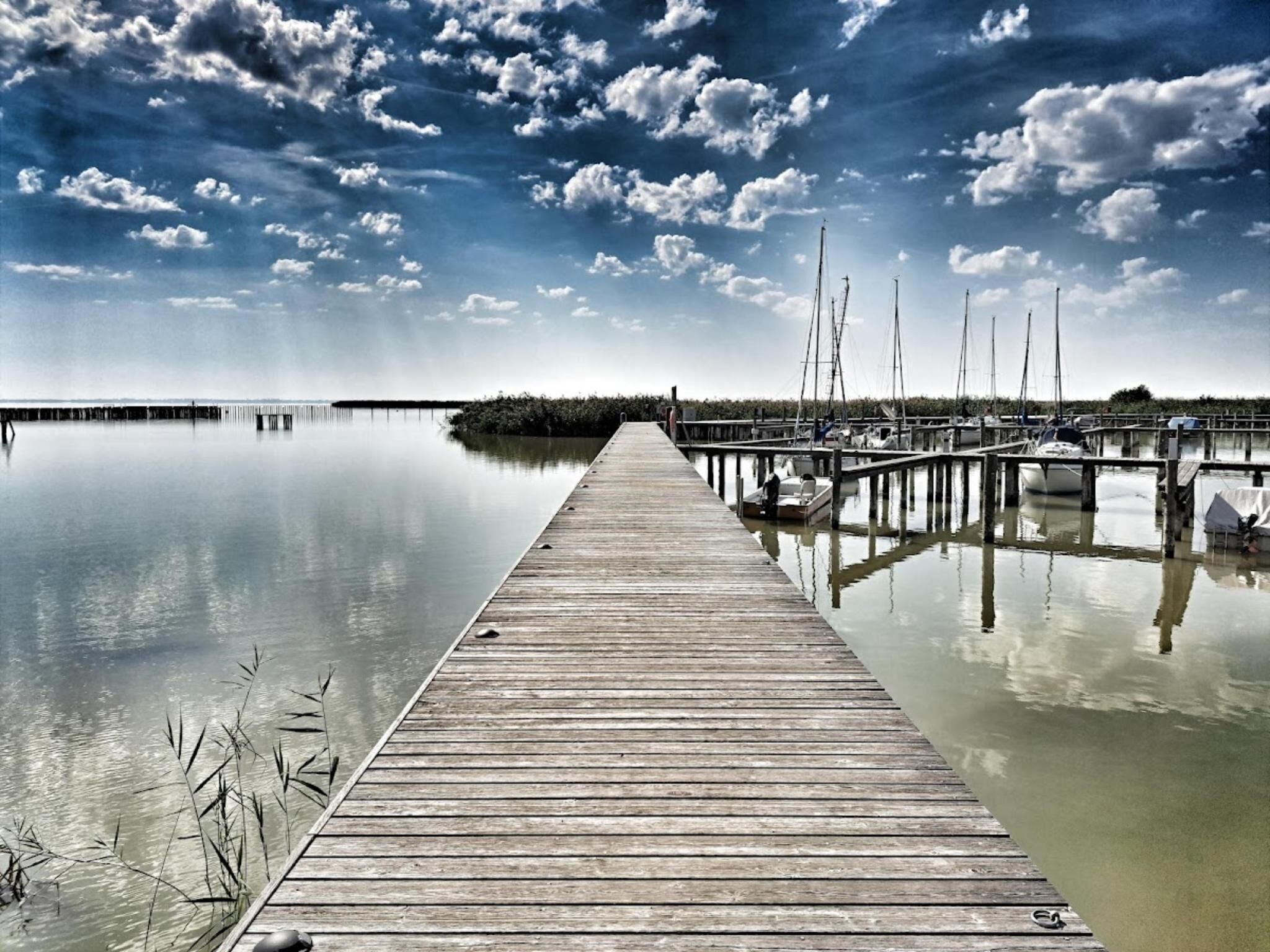 A wooden pier extending into calm water with boats docked on the right.