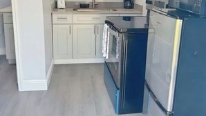 Een kleine keuken met witte kastjes, een roestvrijstalen koelkast en een inbouwoven.