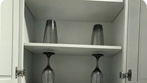 Een keuken met een inbouwplank boven de gootsteen, waarop twee wijnglazen staan. Op de aanrecht hieronder staan een broodrooster en een zwarte mand.