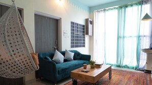 Een woonkamer met een blauwgroene bank, een hangstoel, een houten salontafel en een kleurrijk vloerkleed.