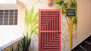Een rode deur met een geometrisch patroon, een bloempot en een muur met een bloemenmuur.