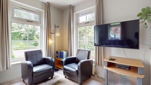 Una sala de estar moderna con dos sillones de cuero, un televisor de pantalla plana, un mueble de madera para entretenimiento y grandes ventanales con vistas a zonas verdes.