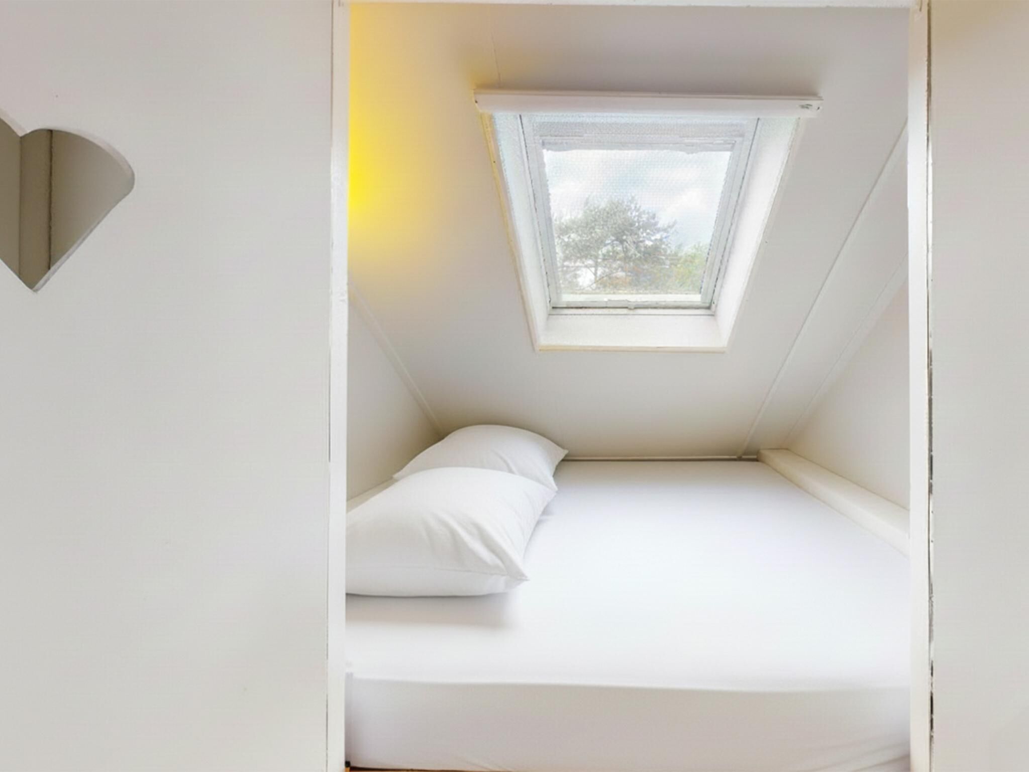 Een kleine, witte slaapkamer in de mansarde met dakraam en een enkel bed.