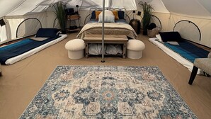 A tented room with a bed, pillows, a small table, and a rug.