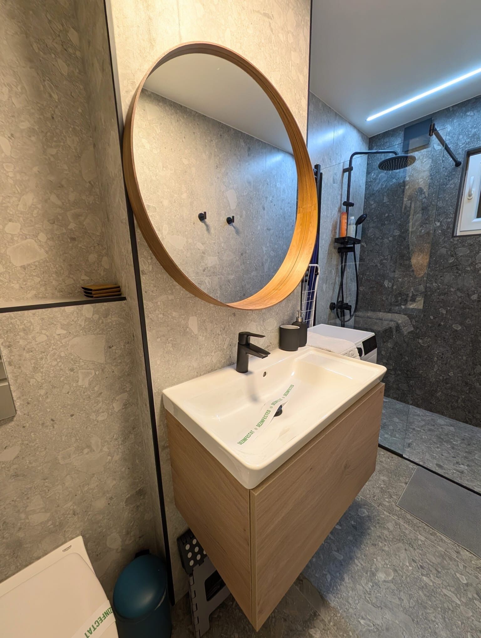 Een moderne badkamer met een houten wastafelmeubel, een ronde spiegel en een douchehoek.