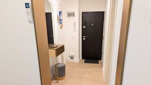 A hallway with a wooden floor, a desk with a chair, a black door, and a wall-mounted intercom. - Imedio Coral Apartment Aviatiei (București)