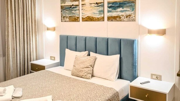 A hotel room with a bed, two bedside tables, a headboard, and three paintings on the wall. - Imedio Coral Apartment Aviatiei (București)