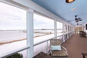 A covered outdoor area with a view of a frozen body of water, wooden deck chairs, and a ceiling fan. - Modern Chesapeake Waterfront - Private Pool - Dock (Cambridge)
