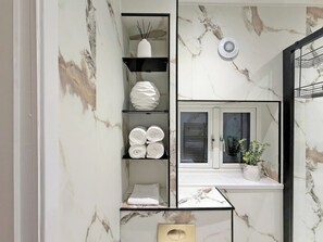 Ein Badezimmer mit Marmorwänden, einem Handtuchhalter, einem Spiegel, einem Fenster mit Pflanze und einem Lüftungssystem.
