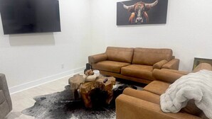 A living room with a brown leather sofa, a mounted flat-screen TV, and a painting of a bull on the wall. - Spring Branch Hill Country Retreat (Canyon Lake)