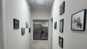 A narrow hallway with white walls and a tiled floor leading to a kitchen area with white cabinets and a refrigerator. - Spring Branch Hill Country Retreat (Canyon Lake)