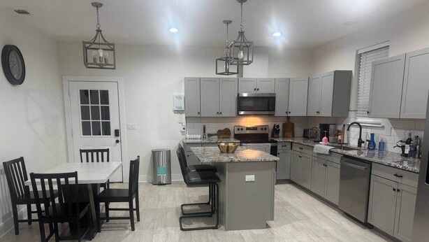 A modern kitchen with grey cabinets, a central island, and a dining area with black chairs. - Spring Branch Hill Country Retreat (Canyon Lake)