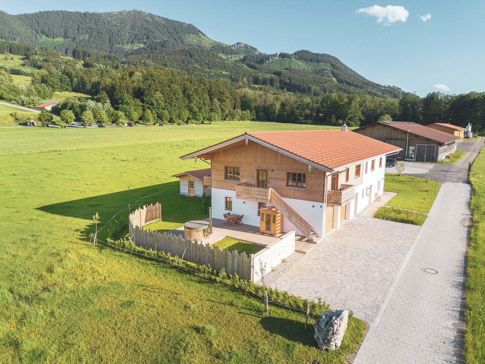 A rural house with a paved driveway, a wooden fence, and a grassy field.