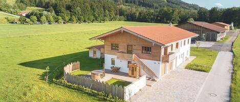A rural house with a paved driveway, a wooden fence, and a grassy field.