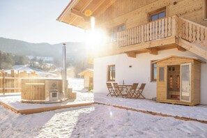 Een houten chalet met balkon, een jacuzzi en een tafel met stoelen buiten.