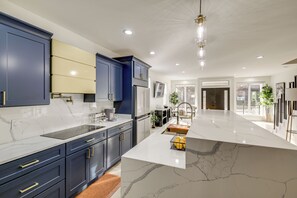 A modern kitchen with dark blue cabinets, a white marble island, and stainless steel appliances.